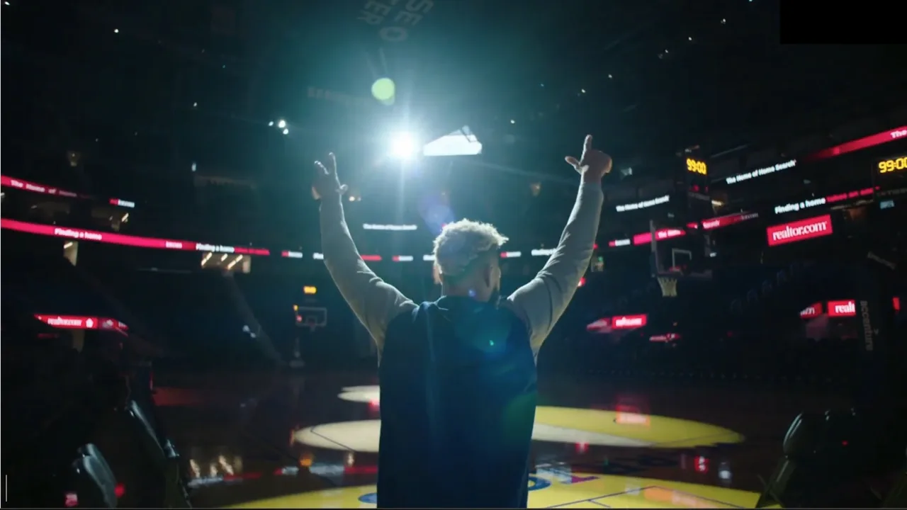 A player stands on a basketball court under arena lights with arms raised, in a frame from Nick Schwyter's Steadicam reel.